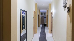 Ein Flur mit Türen an beiden Seiten, einem gefliesten Boden und einer Leuchte an der rechten Wand.