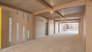 Un pasillo espacioso con piso de ladrillo, ventanas grandes y techo alto.