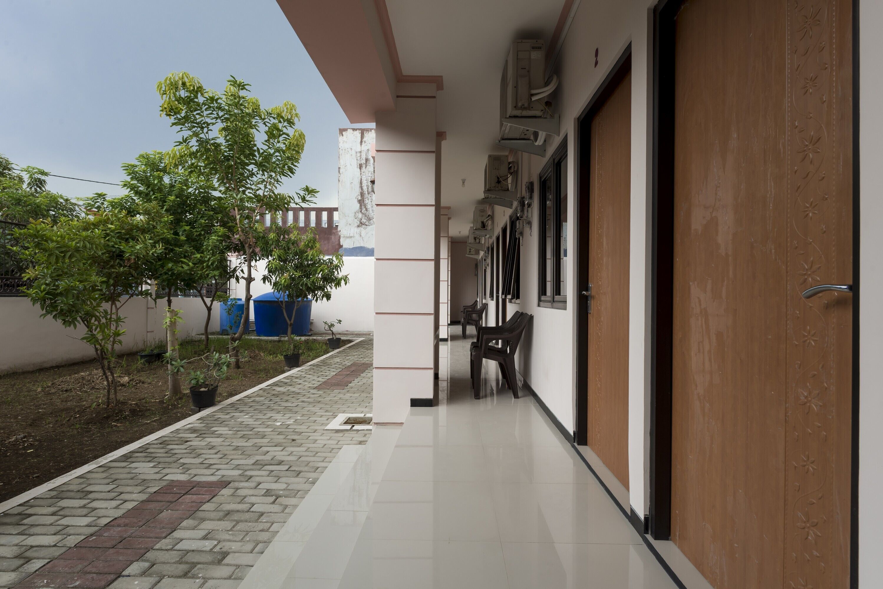 A corridor with tiled flooring, potted plants, and a bench. - KoolKost Syariah near UPN Veteran (Surabaya)