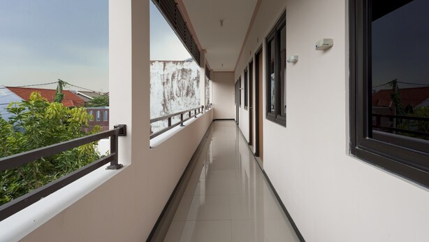A corridor with a balcony, large windows, and a view of buildings. - KoolKost Syariah near UPN Veteran (Surabaya)