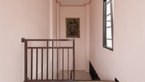 A narrow hallway with a wooden railing, a painting on the wall, and a window on the right. - KoolKost Syariah near UPN Veteran (Surabaya)