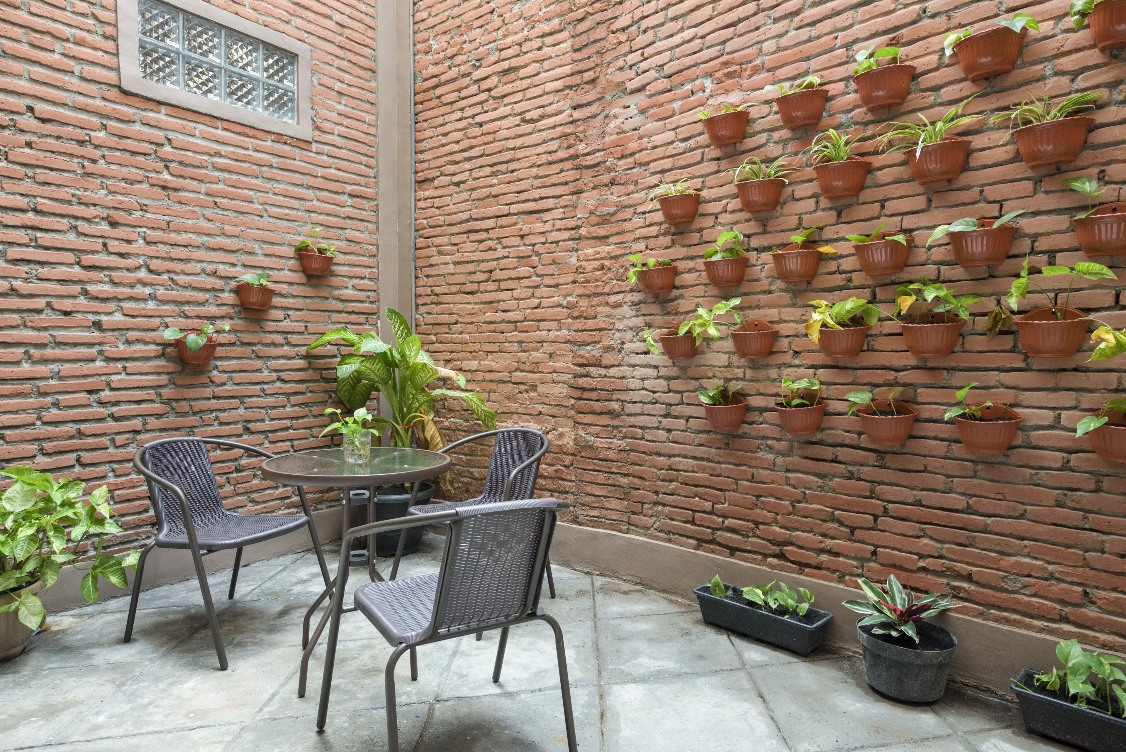 A brick-walled patio with a round table and chairs, surrounded by potted plants.