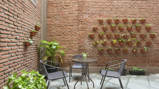 A brick wall with potted plants arranged in a grid pattern. There are two metal chairs and a small round table in the foreground. - RedDoorz Hostel near Malang Train Station 3 (Malang)