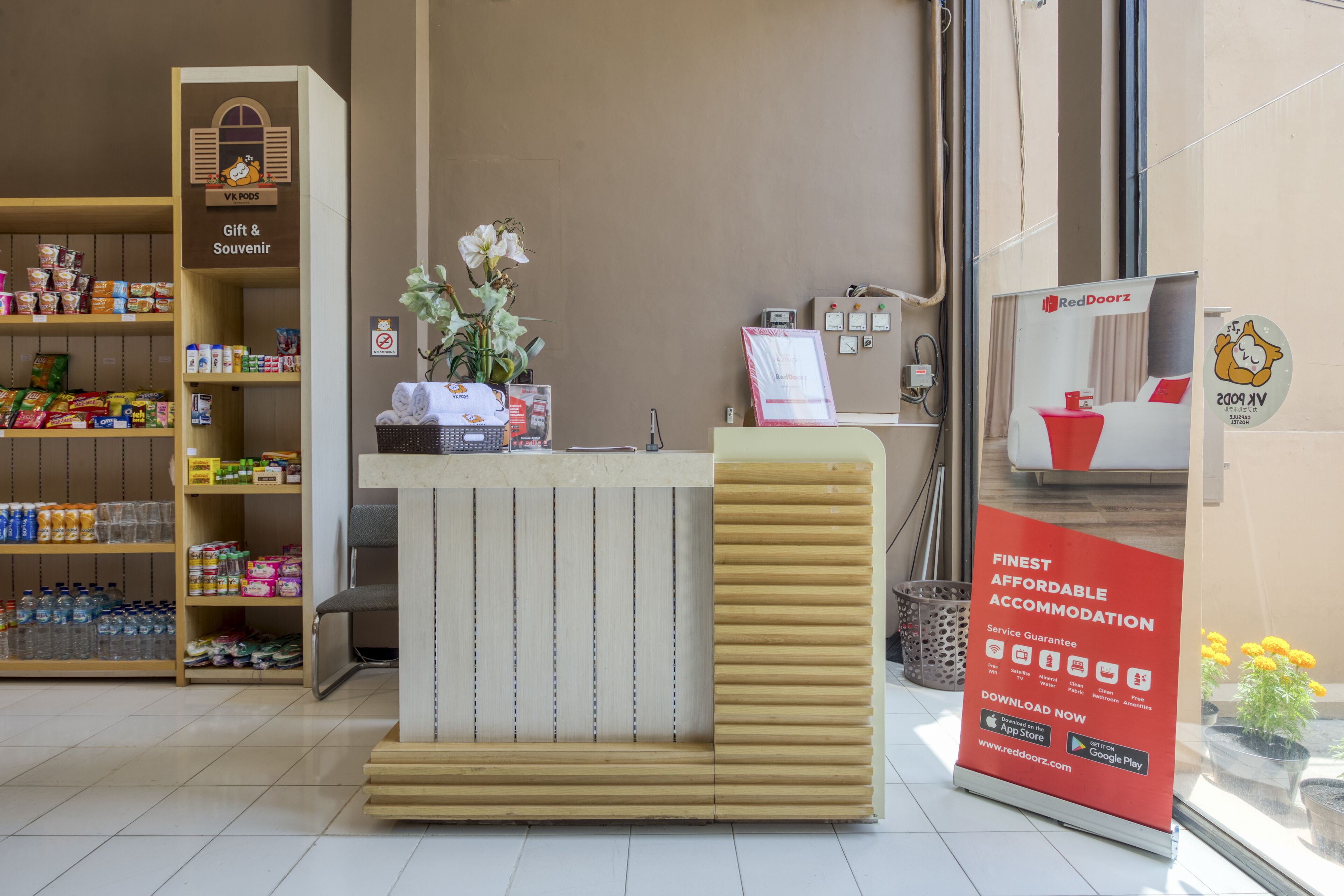 Un espace d’accueil d’hôtel avec un comptoir en bois, un rayon de cadeaux et de souvenirs, et une enseigne RedDoorz.