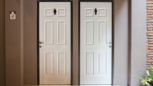 Two white doors with a no-smoking sign above them, a tiled floor, and a potted plant to the right. - RedDoorz Hostel near Malang Train Station 3 (Malang)