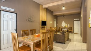 A dining area with a wooden table and chairs, a television mounted on the wall, and a sofa in the background. - RedDoorz Hostel near Malang Train Station 3 (Malang)