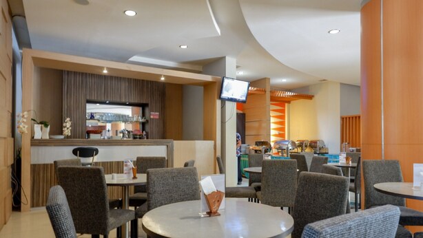 Um saguão moderno de hotel com área de bar, assentos e uma tela de televisão.