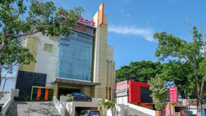 Hotel moderno com fachada de vidro imponente, um carro estacionado em frente e uma escadaria que leva à entrada.