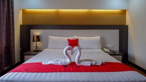 Quarto de hotel com cama, manta vermelha, travesseiro, luminária e telefone fixado na parede.