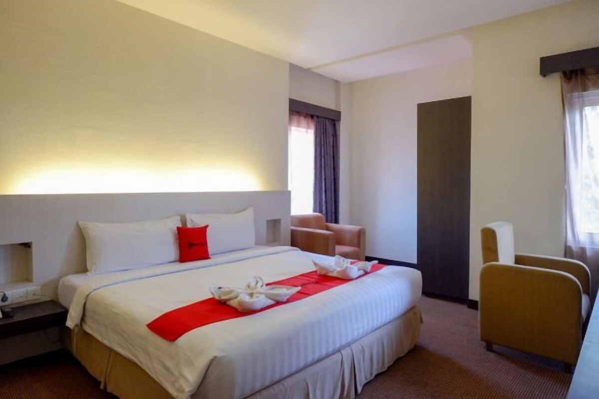 A hotel room with a large bed, a desk, a chair, and a window.