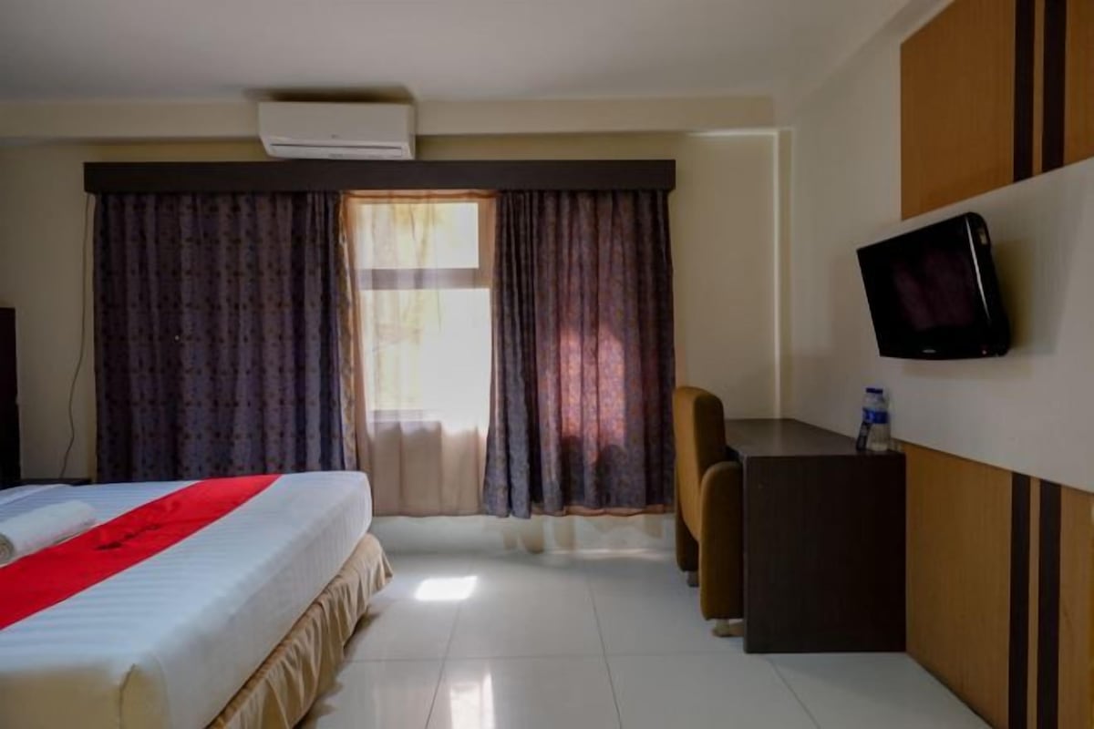 Une chambre d’hôtel avec un lit, un bureau, une chaise, une télévision et une fenêtre avec des rideaux.