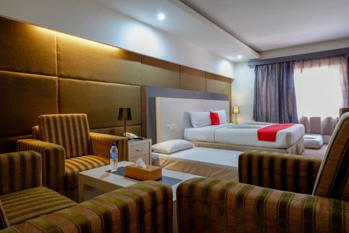 Habitación de hotel con cama, dos sillones, una mesita de noche y una ventana con cortinas.