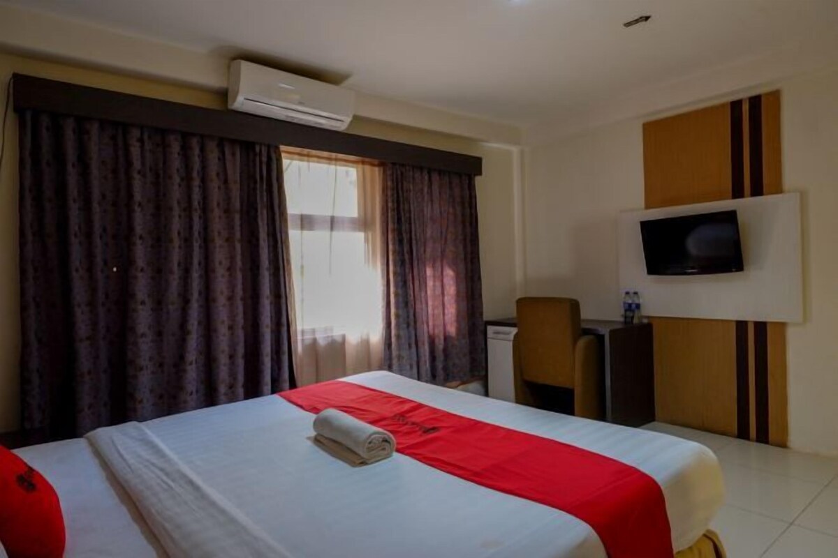 Una habitación de hotel con una cama, cortinas, televisor y escritorio.
