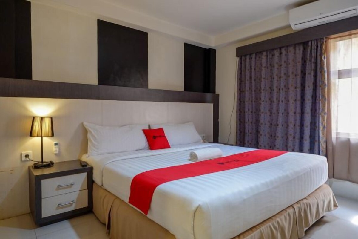 A hotel room with a bed, a nightstand, a lamp, and a window with curtains.