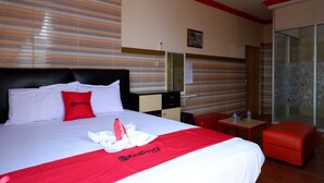 Habitació d'hotel amb llit, escriptori, cadira i un panell de vidre.