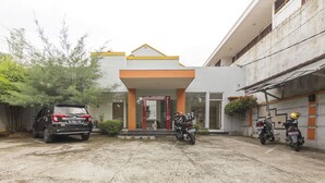 A building with a central entrance, a car, and three motorcycles parked in front. - KoolKost Syariah @ Jalan Sisingamangaraja Semarang (Semarang)