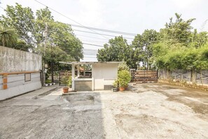 Un patio con una zona de estar techada y de tamaño reducido, plantas en macetas y suelo de hormigón.
