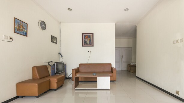 A modern living room with a brown leather sofa, a coffee table, and a television. There are wall-mounted clocks and framed pictures. - KoolKost Syariah @ Jalan Sisingamangaraja Semarang (Semarang)
