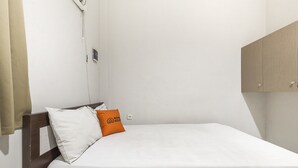 A single bed with white bedding and two pillows, one white and one orange, in a room with a wooden headboard and a light-colored wardrobe. - KoolKost Syariah @ Jalan Sisingamangaraja Semarang (Semarang)