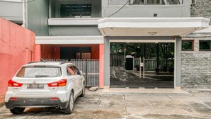 Une voiture blanche est garée devant un immeuble dont l’entrée est protégée par un portail et qui est bordé d’un mur en pierre.