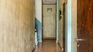 Un couloir étroit, avec une porte en bois sur la droite et un mur bleu sur la gauche.