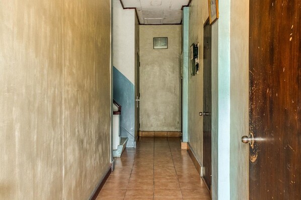 A narrow hallway with a wooden door on the right and a blue wall on the left. - RedDoorz near Plaza Senayan (Jakarta)