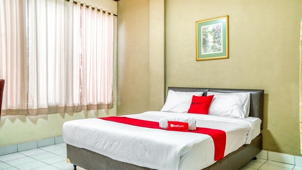 Une chambre d’hôtel avec un lit, des rideaux, un tableau encadré au mur et une serviette rouge sur le lit.