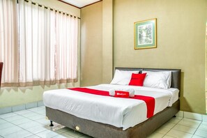 A hotel room with a bed, curtains, a framed picture on the wall, and a red towel on the bed. - RedDoorz near Plaza Senayan (Jakarta)