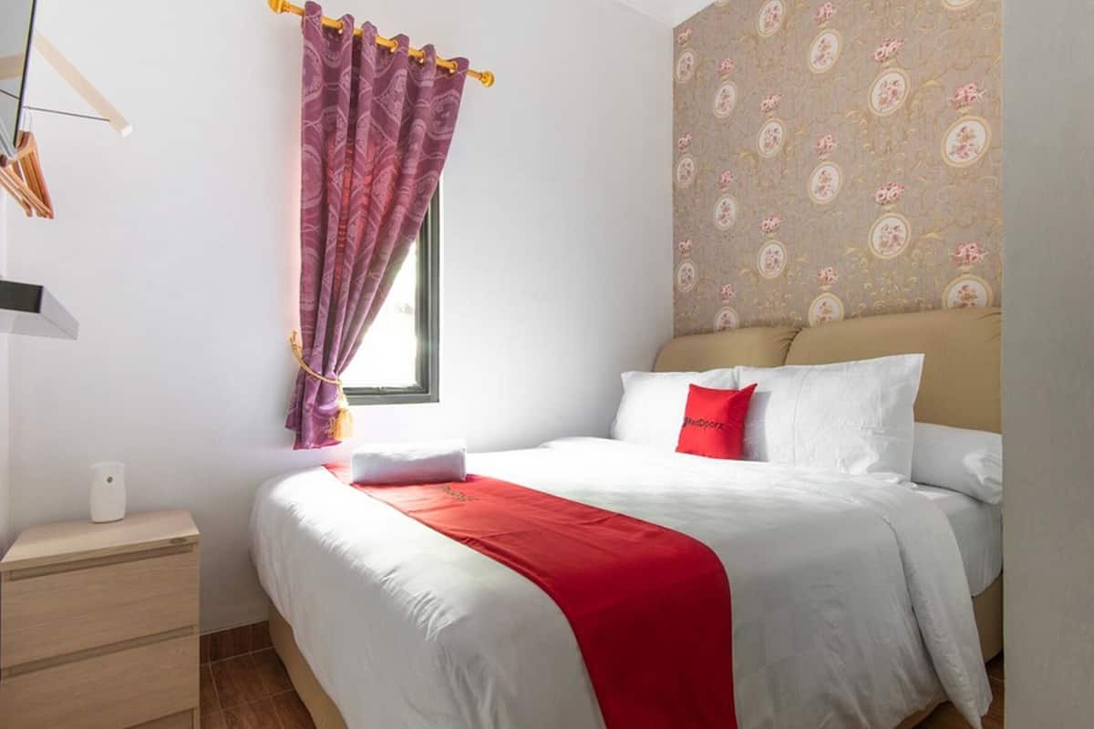 A neatly made bed with white and red bedding, a bedside table with a lamp, and a patterned wallpaper on the wall.