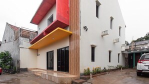 A modern two-story house with a flat roof, a balcony with yellow railings, and a small front porch. - RedDoorz Plus near Trans Studio Cibubur 2 (Bekasi)