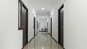 A long, narrow hallway with dark doors on both sides and a shiny, reflective floor. - RedDoorz Plus near Trans Studio Cibubur 2 (Bekasi)