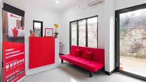 A modern hotel lobby with a red sofa, large windows, and a RedDoorz advertisement. - RedDoorz Plus near Trans Studio Cibubur 2 (Bekasi)