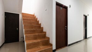 A modern interior with a wooden staircase leading to a dark wooden door, white walls, and a tiled floor. - RedDoorz Plus near Trans Studio Cibubur 2 (Bekasi)