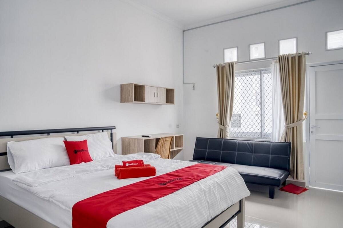 Une chambre d’hôtel avec un lit, une banquette, un bureau et une fenêtre avec des rideaux.