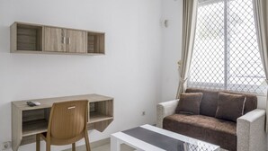 Une pièce comprenant un bureau, une chaise, un canapé et une fenêtre avec des rideaux.