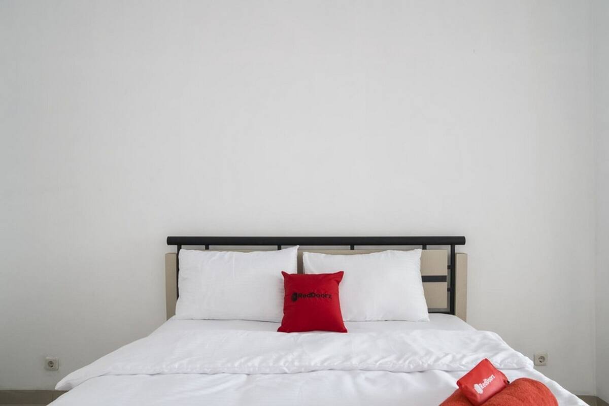 Un lit avec une literie blanche et deux oreillers rouges, dont l’un porte un logo.