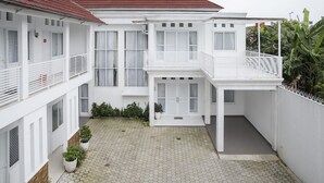 Un bâtiment blanc à deux étages, avec un toit rouge, une terrasse couverte et une cour dallée.