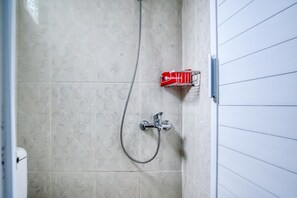 Een badkamer met een douche, een rode zeepdispenser en een handdoekhouder aan de muur.