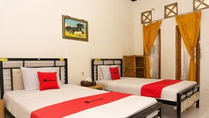 Two single beds with white bedding and red accents, a wooden wardrobe, and a painting on the wall.