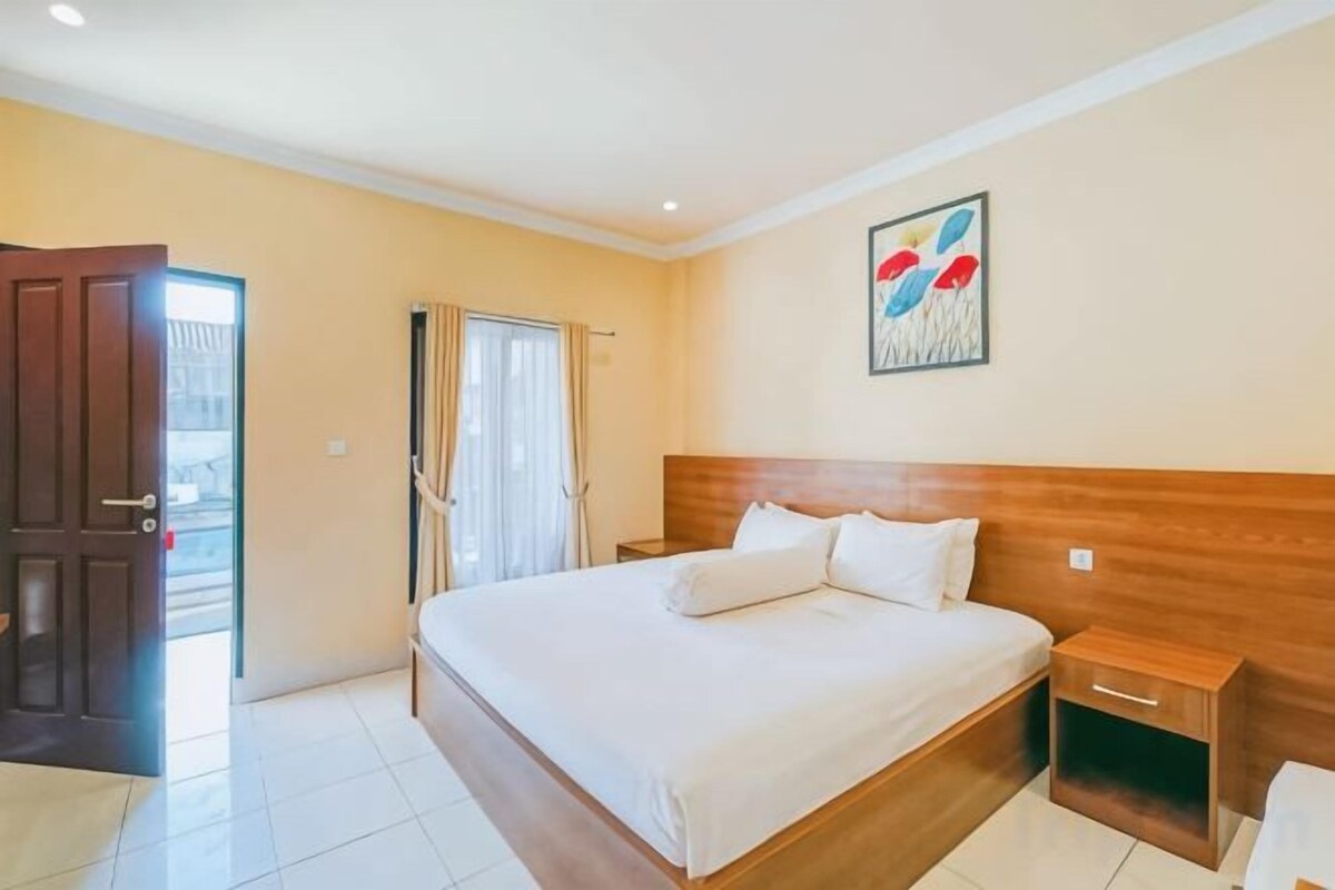 Une chambre d’hôtel avec un grand lit, une tête de lit en bois, une table de chevet et une porte donnant sur un balcon.