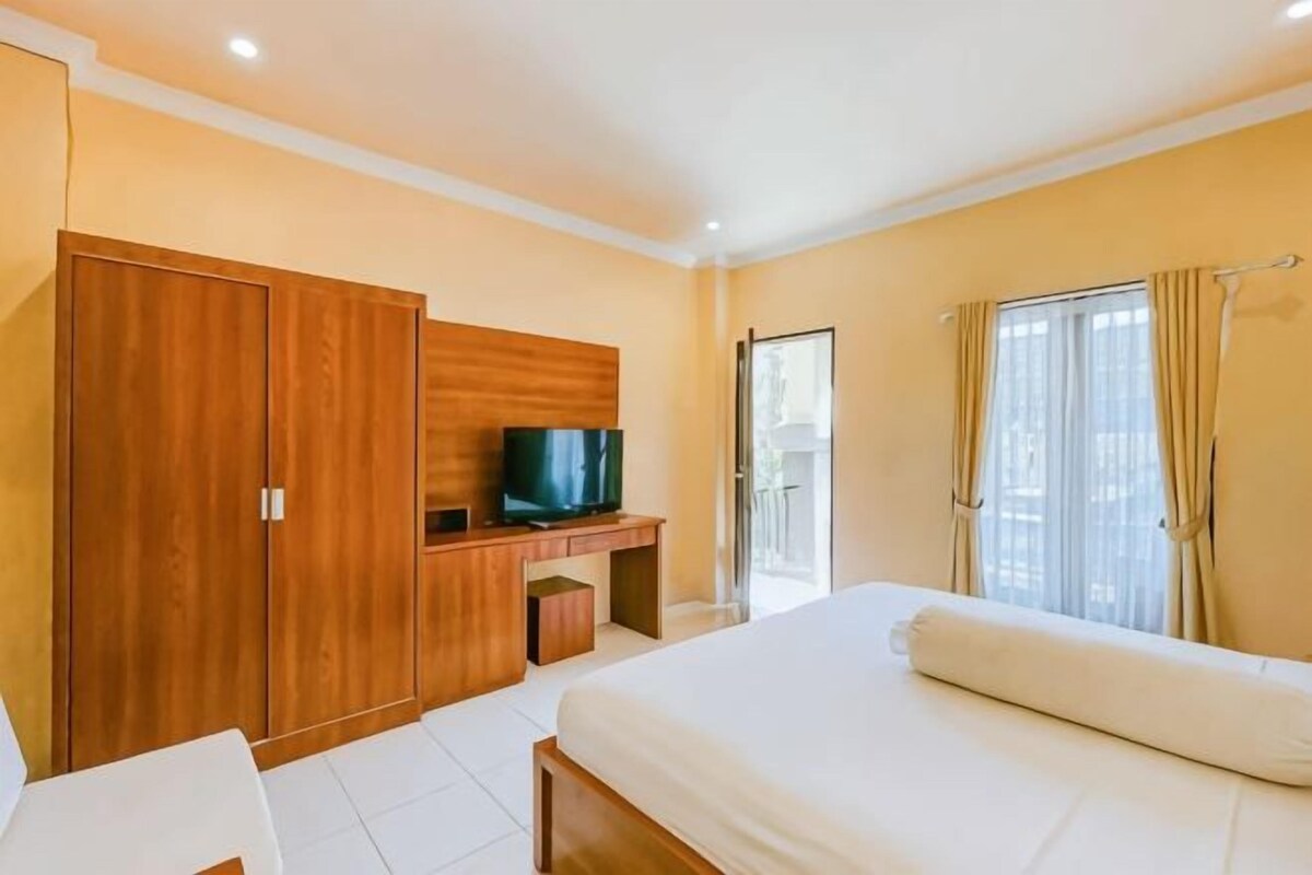 A hotel room with a bed, a TV, a wardrobe, and a window with curtains.