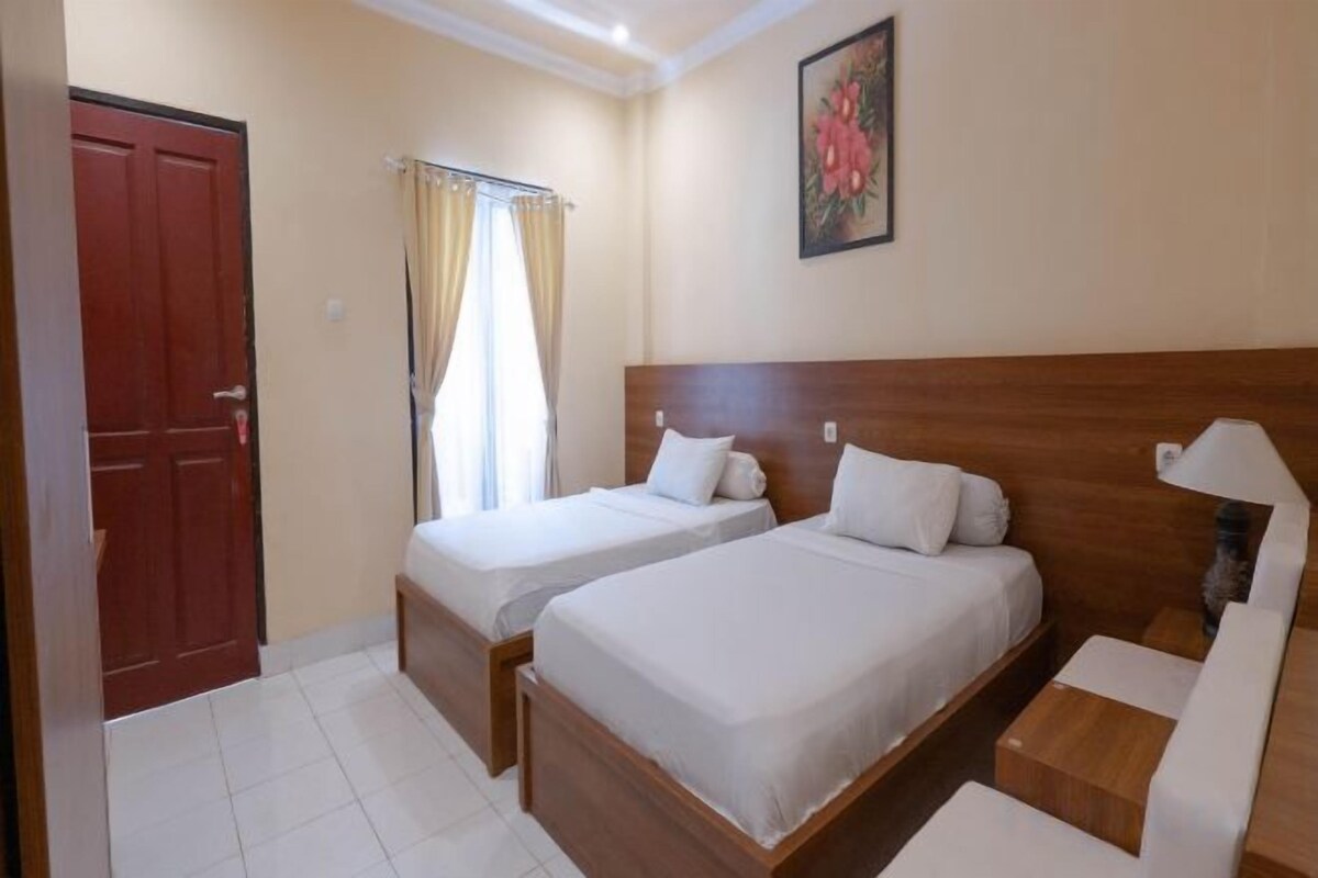 A hotel room with two beds, a wooden headboard, a bedside table, and a door.