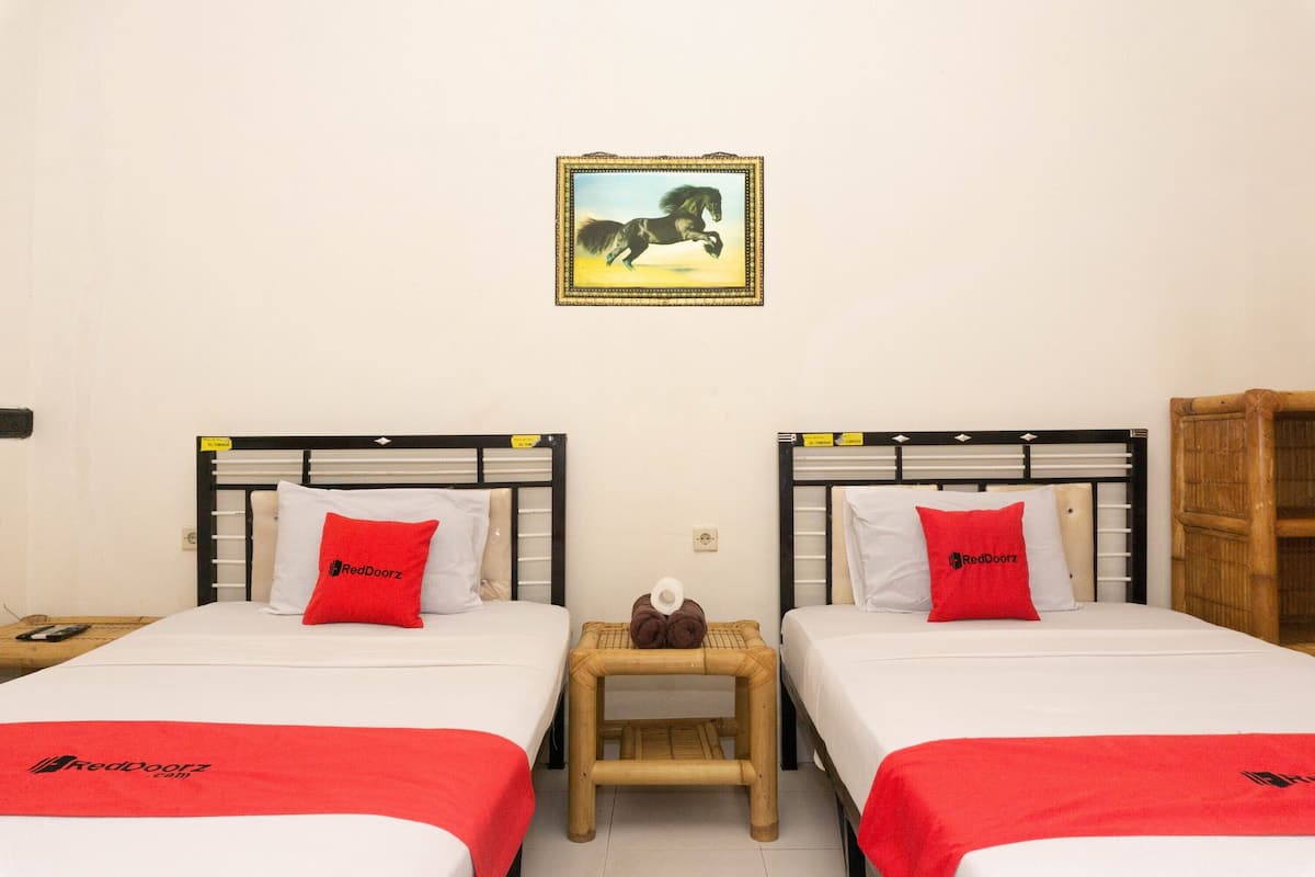 Ein Hotelzimmer mit zwei Betten, jeweils mit roter Decke und Kopfkissen, einem kleinen Nachttisch und einem gerahmten Bild an der Wand.