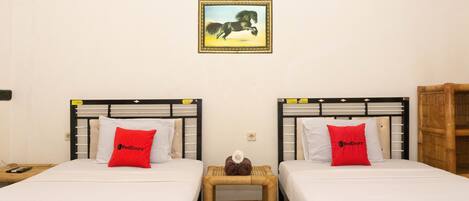 A hotel room with two beds, each with a red blanket and pillow, a small wooden nightstand, and a framed picture on the wall.