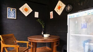 A corner with a wooden chair, a small round table with a plant and a bottle, and a refrigerator with beverages.