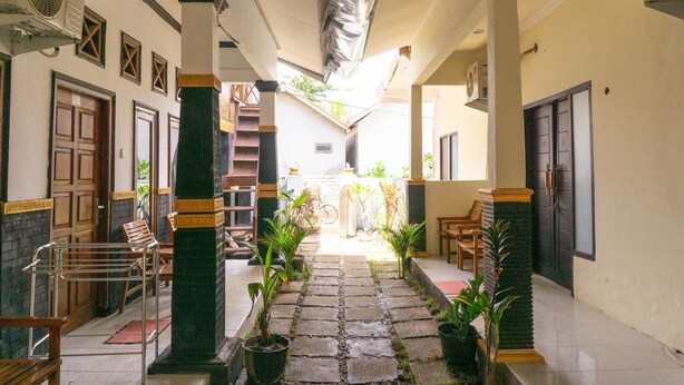 A corridor with stone flooring, potted plants, wooden benches, and doors leading to rooms.