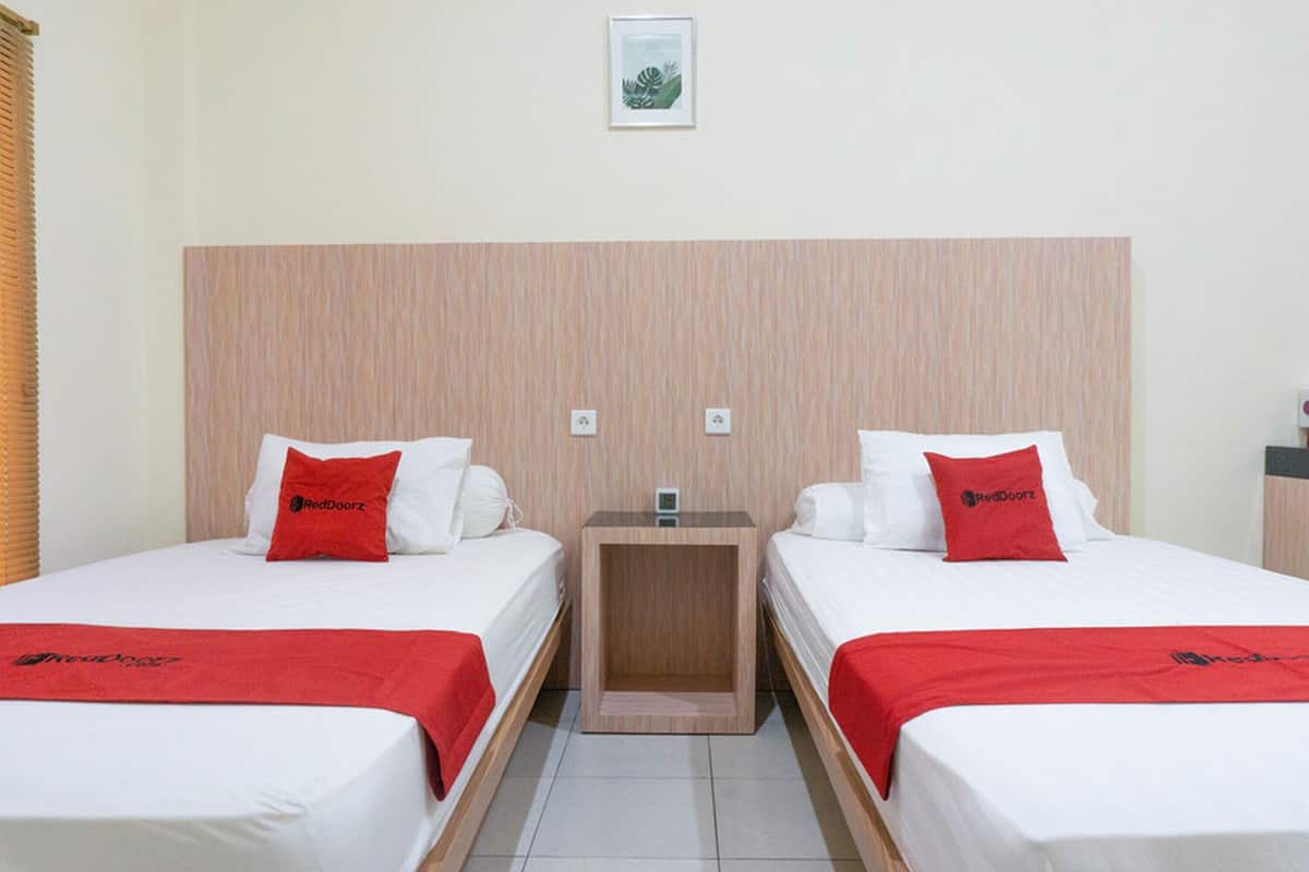 Habitación de hotel con dos camas individuales, cada una con una almohada roja y una manta a juego.