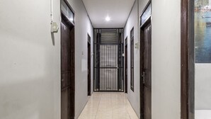 A corridor with tiled flooring, dark wooden doors, and a view of a water body through a window. - RedDoorz @ Jemursari Surabaya 2 (Surabaya)