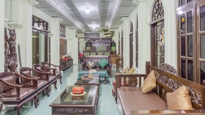 A spacious room with a long wooden sofa, a glass coffee table, and a wooden chair. There is a bookshelf filled with books and decorative items. - RedDoorz Syariah @ Lempuyangan (Yogyakarta)