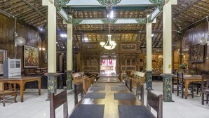 A long dining table with chairs, surrounded by ornate wooden pillars and a high ceiling with intricate designs. - RedDoorz Syariah @ Lempuyangan (Yogyakarta)